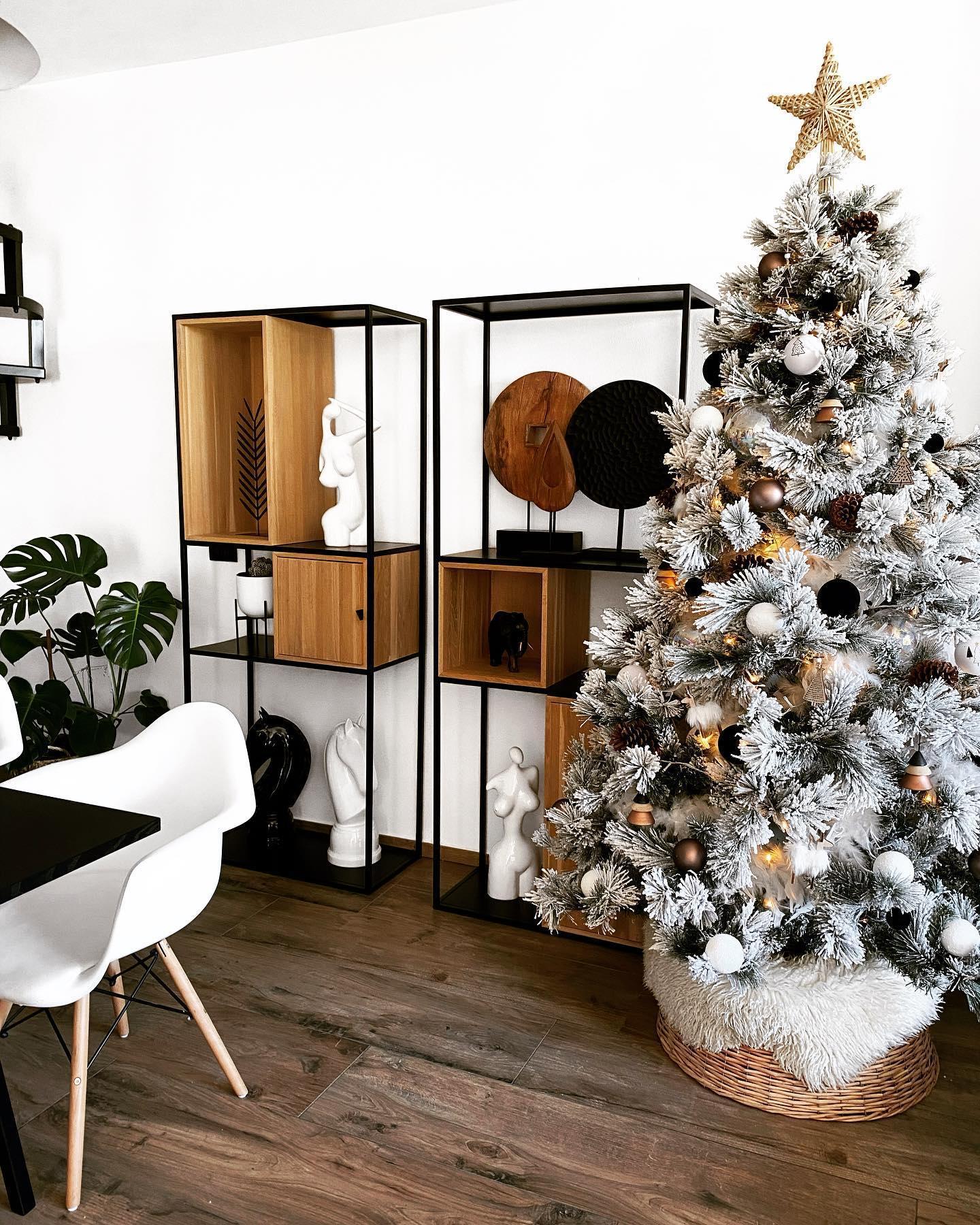 Choinka oprószona sztucznym śniegiem ze złotymi i miedzianymi ozdobami obok industrialnego regału