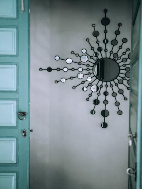 Przeszklone drzwi w turkusowym kolorze, na ścianie za drzwiami dekoracyjne lustro z czarną ramą