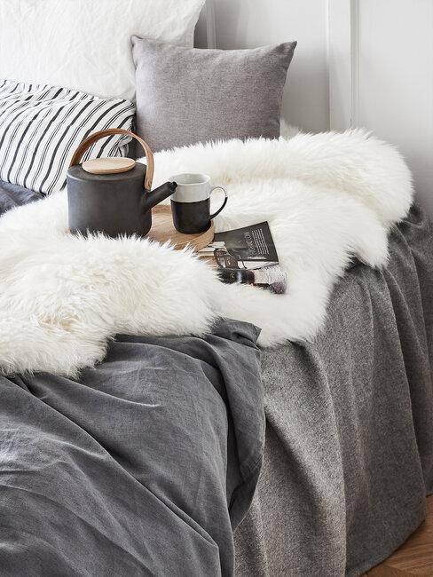 szara sypialnia: tekstylia w kolorze szarym, na łózku biały pluszowy koc i taca z dzbankiem i kubkami