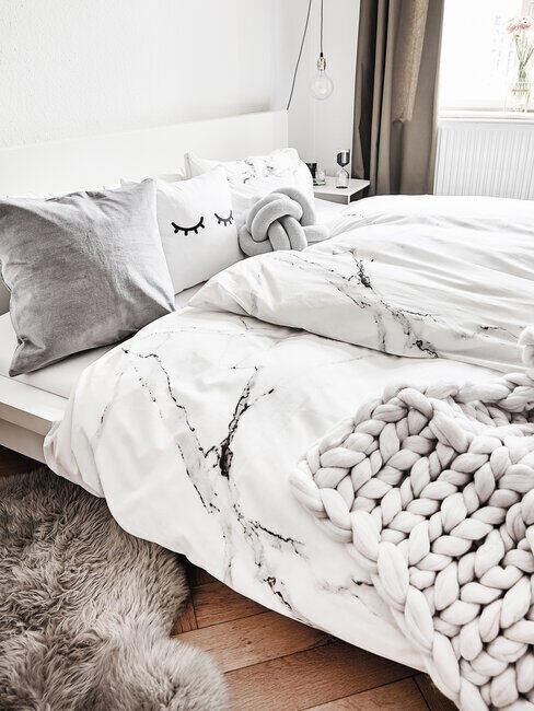 szara sypialnia: szare tekstylia w sypialni z drewnianym łożkiem bez wezgłowia