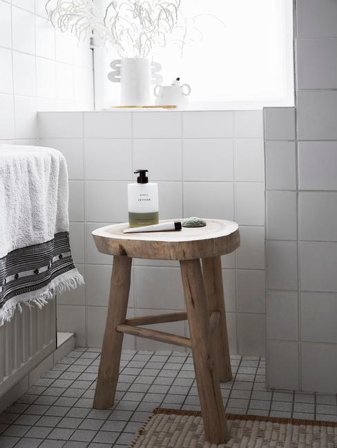 Drewniany stołek okrągły w łazience z białymi płytkami i czarna fuga na podłodze