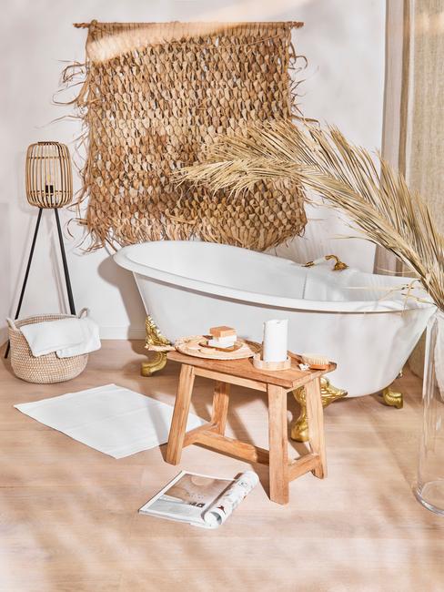 Biała wolnostojąca wanna, w łazience z bezowymi płytkami na podłodze i dodatkami w stylu boho