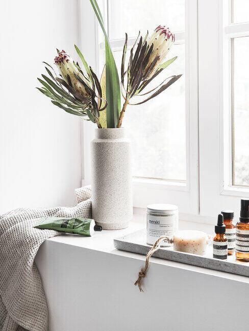 Kwiaty stojące na oknie w szarej łazience, obok kosmetyki