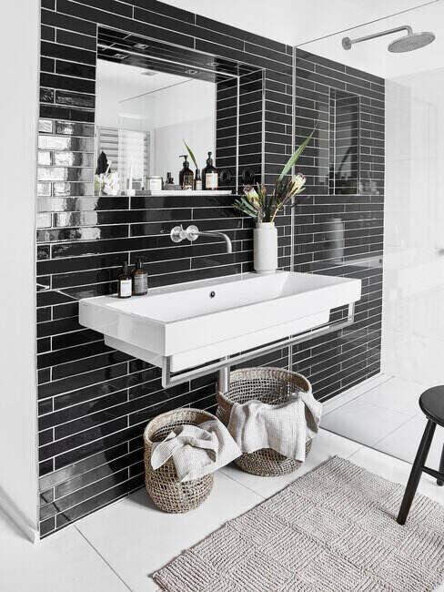 Biała umywalka przymocowana do ściany z czarnymi płytkami