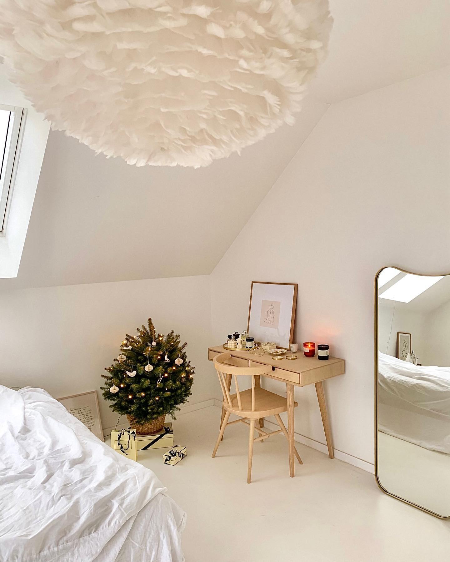 Sypialnia na poddaszu z małym biurkiem drewnianym i lampą z piór