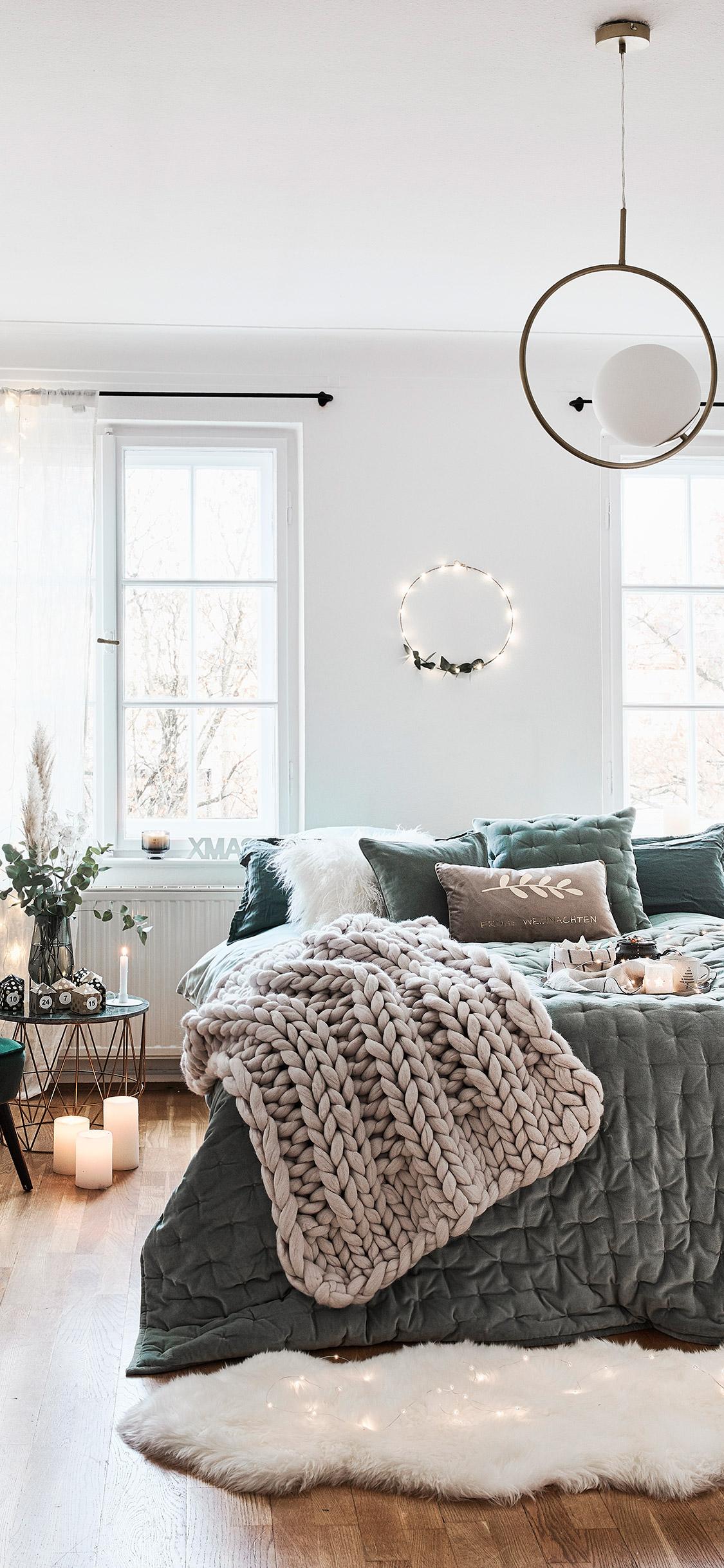 tapeta na telefon przedstawiająca przytulne łóżko z zieloną narzutą i lampkami