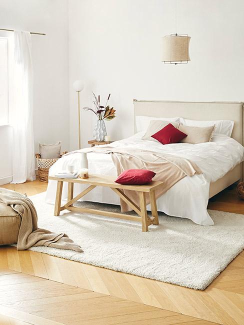 Jasna sypialnia w stylu boho z drewnianymi meblami i ciemno czerwonymi poduszkami