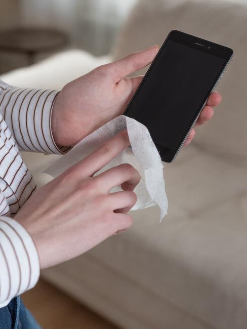 Dłonie trzymające telefon i przecierające ściereczką