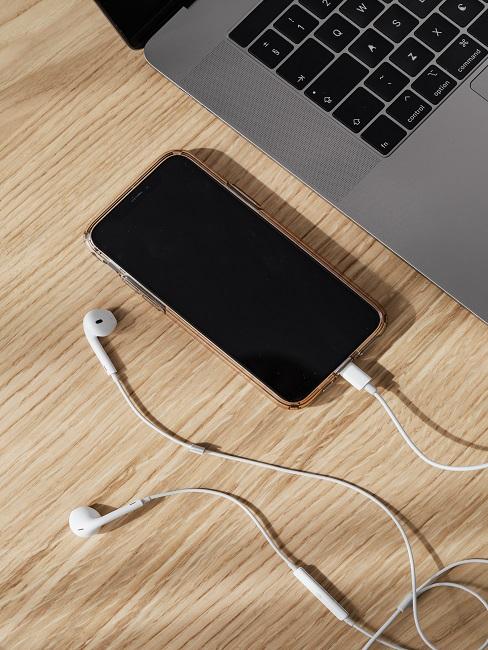 Podłączone słuchawki do telefonu obok laptopa na drewnianym stole