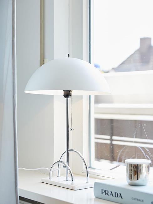 Sytlowa lampa z białym kloszem na srebrnej podstawie na parapecie