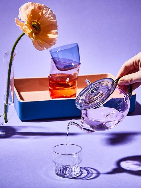 fioletowy imbryk do herbaty na tle kolorwej tacy i żółtego kwiata