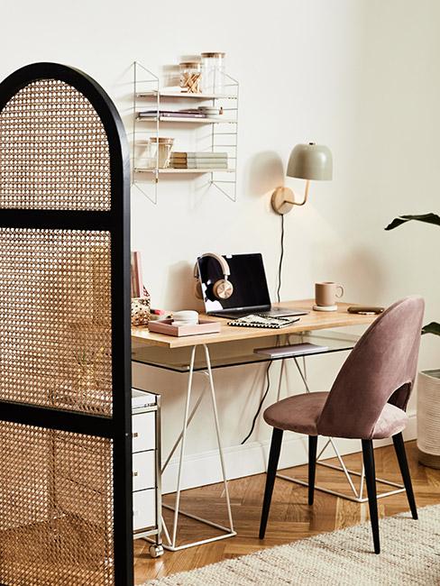 małe biurki przy krześle w stonowanym różu przy drewnianym biurku pod ścianą za parwanem