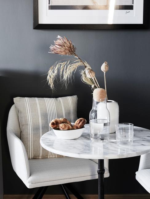 mały stolik do jadalni z marmuru przy białym krześla z podłokietnikami na tle ciemnoszarej ściany