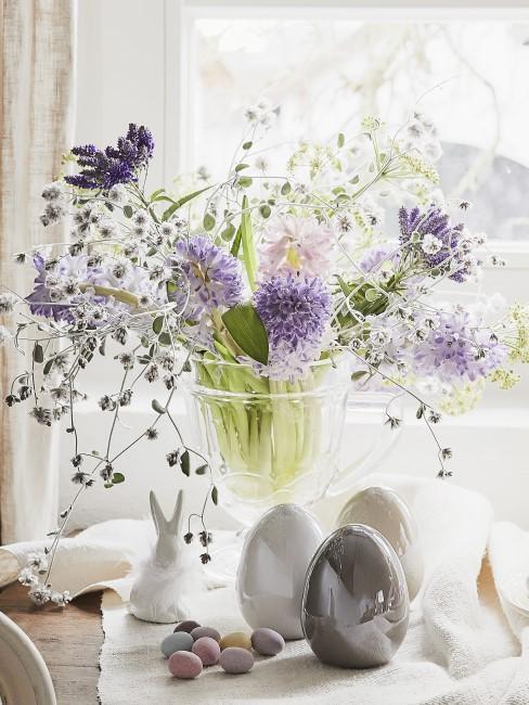 wazon z fioletowymi kwiatami obok dekoracji wielkanocnych