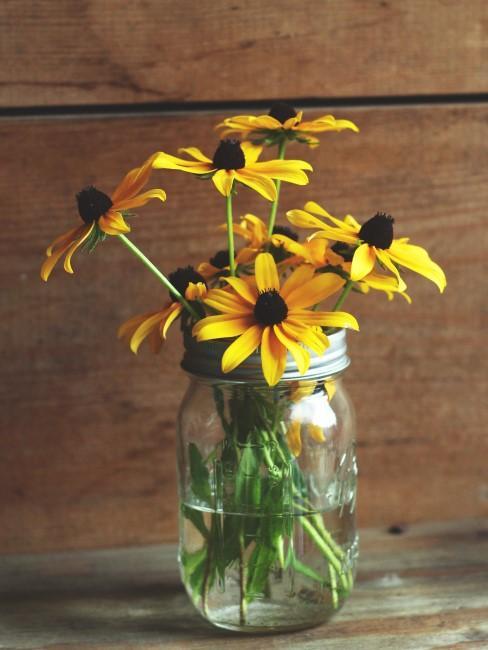 Żółte kwiaty w wazonie na tle drewnianej ściany