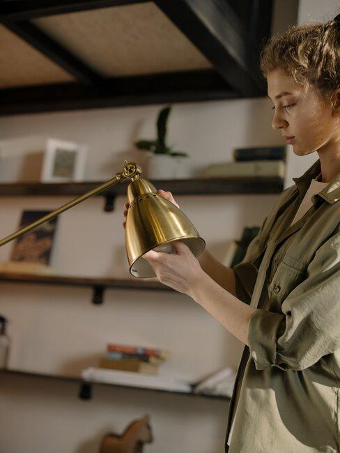 kobieta wymieniająca żarówkę w złotej lampce