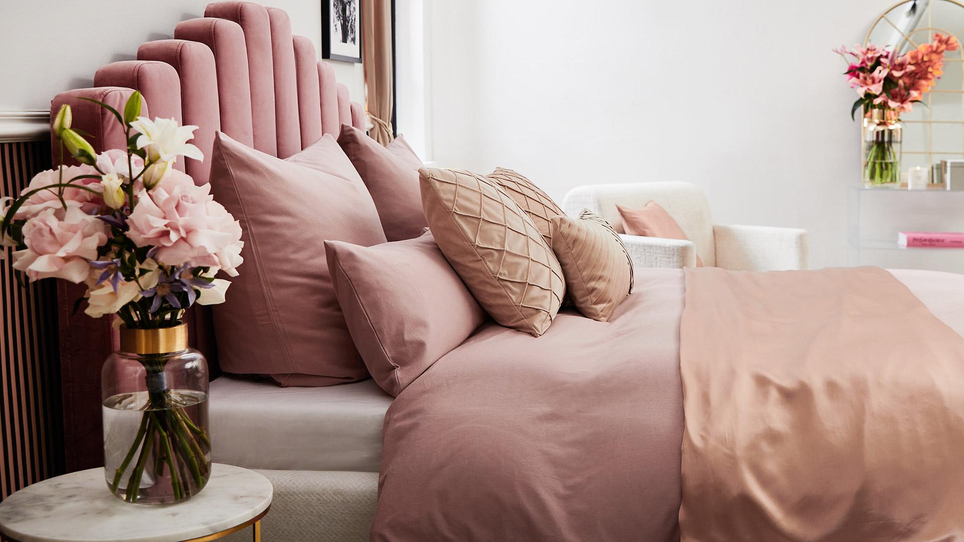 tapeta wiosenna na pulpit przedstawiająca różowe łóżko z aksamitu z różowóą pościelą obok stolika nocnego z bukietem kwiatów