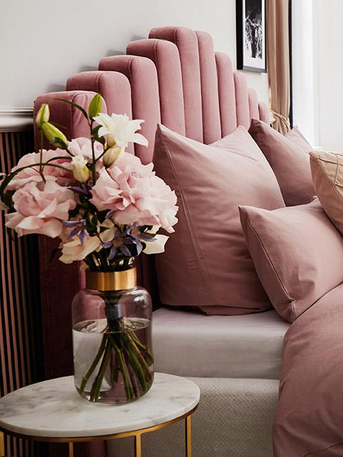 piękny bukiet róż w szlanym wazonie ze złotą obręczą obok łóżka z różowym zagłówkiem z weluru