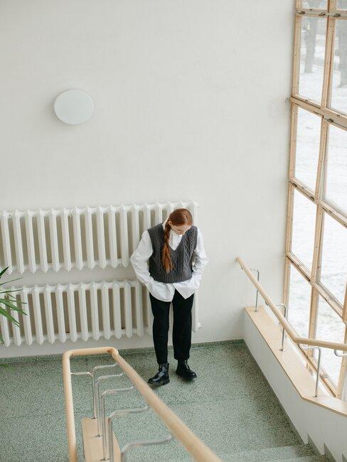 kobieta stojąca na klatce schodowej w stylu socrealistycznym obok kaloryfera