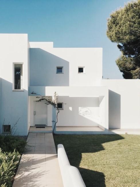 biały, nowoczesny, minimalistyczny dom z równo skoszonym trawnikiem