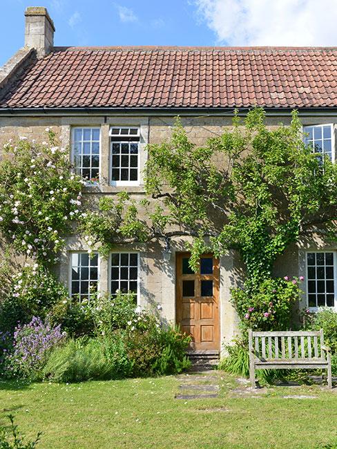 ogródek przed domem w stylu angielskim z roślinami pnącymi i ławeczką