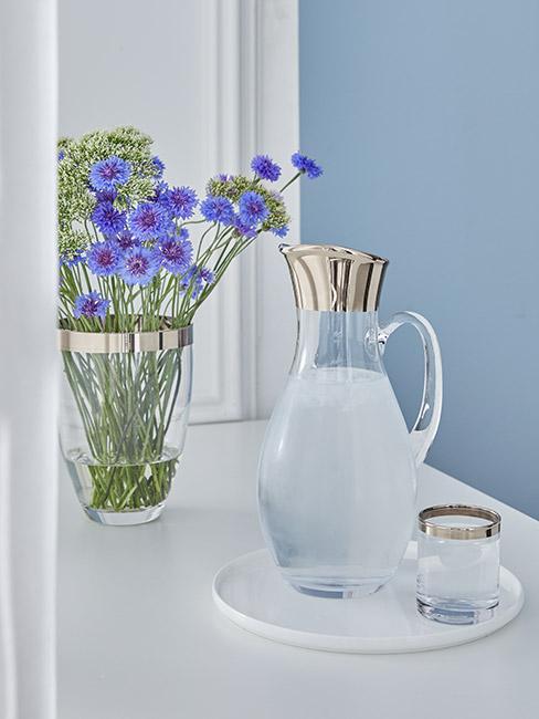 kolor błękitny na ścianie w kuchni za szklaną karafką wody obok wazonu z chabrami