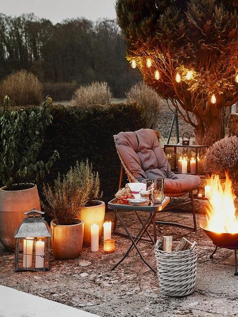 palenisko, a przy nim fotel i stolik ogrodowy, dookoła lampiony i światełka
