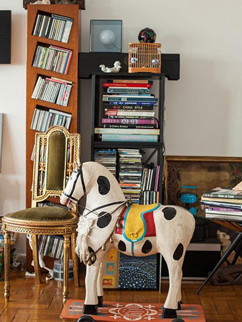 kreatywna biblioteczka w salonie z książkami ustawionymi na regałach o ciekawych kształtach obok konia na biegunach