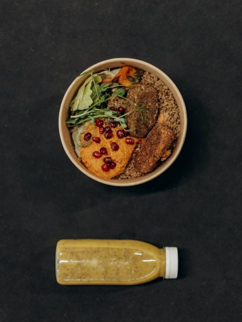 poke bowl na czarnym tle, a obok żółty sok w butelce