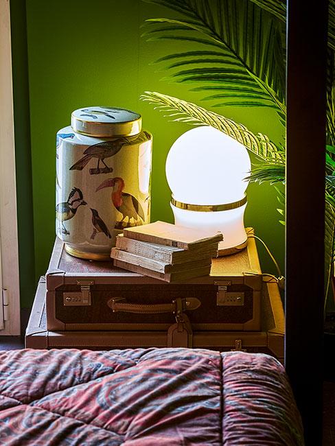 lampka nocna na starej walizce na tle zielonej ściany