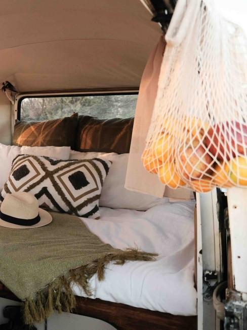 kamper z łóżkiem i poduszkami w stylu boho i obok siatka materiałowa z owocami