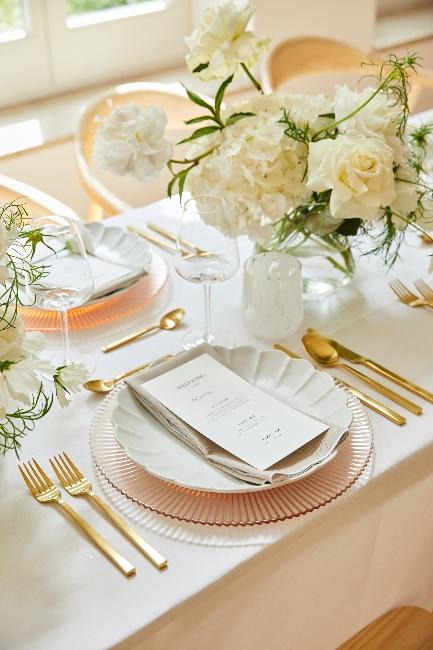 Elegancko nakryty stół ślubny białą zastawą i złotymi sztućcami