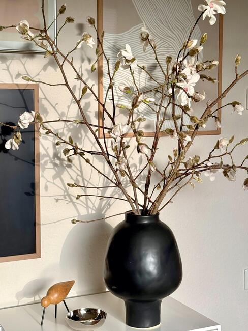 Kwitnące gałązki w czarnym wazonie na komodzie
