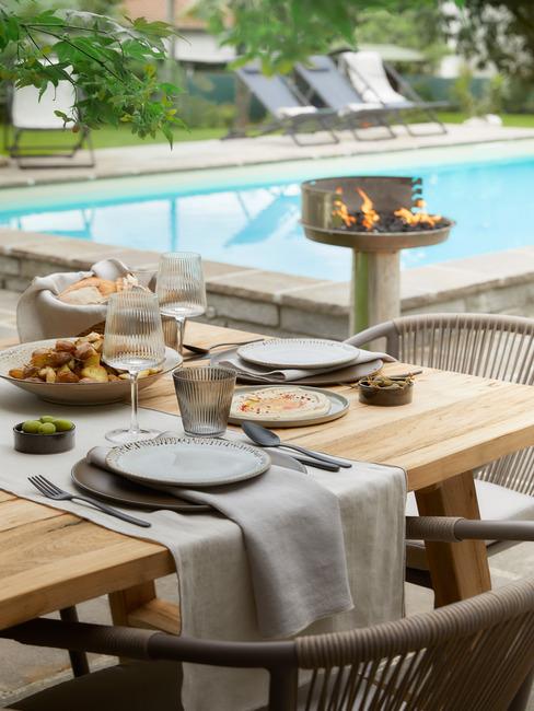 Drewniany stół na tarasie przy basenie nakryty do grilla