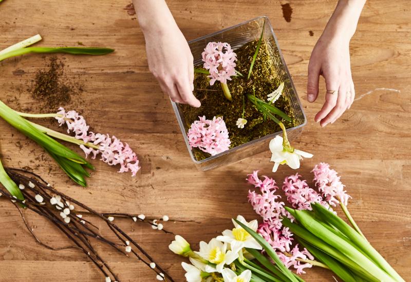mains qui créent une decoration de table faite de mousse et de fleurs