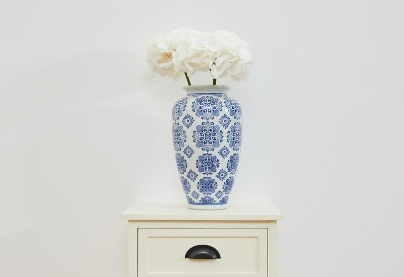 witte kast met een wit met blauwe bloemenvaas en witte bloemen