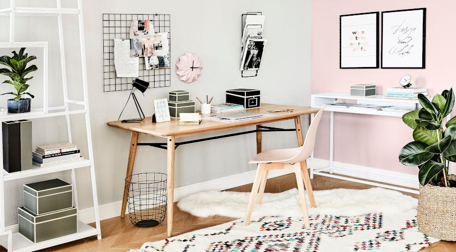 een hout bureau en stoel in een kantoor met roze muur en boho kleed