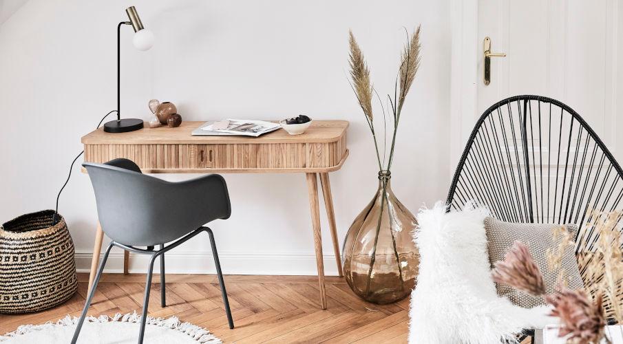Retro bureau van licht hout met een grijze stoel en naast een grote vaas met veren