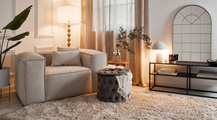 Opbergbox rond met een deken er in ennaast een grijze fauteuil en zwarte sidetable met witte lamp