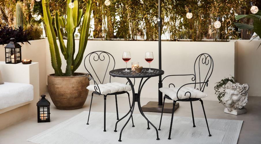 Beton schutting achter een cactus en metalen bistroset met wijnglazen er op