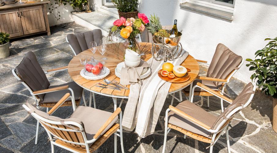 Ronde houten tuintafel met vier houten stoelen en een gedekte tafel met mooie bloemen