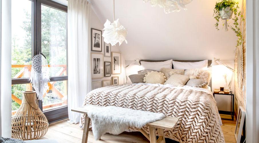 beige dekbedovertrek en kussens in een boho slaapkamer met een plant en groot raam