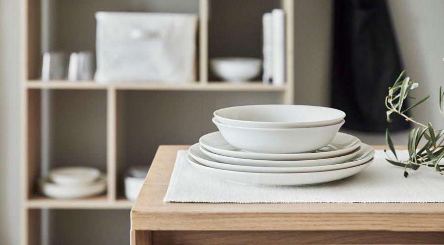 wit scandinavisch servies op een houten keukentafel en met een kast in de achtergrond