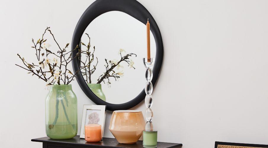 zwarte ronde spiegel boven een dressoir met een vaas bloemen, decoratie en een kaars