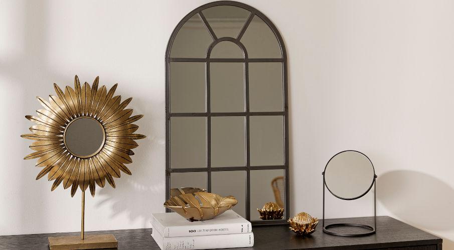 Industriële spiegel en goude accessoires op een zwart dressoir