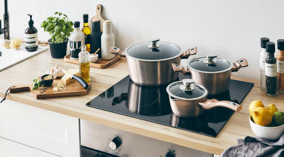 Kookpannenset van drie pannen in een witte keuken met houten aanrecht