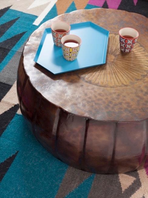 Runder Couchtisch aus Holz auf einem Ethno Teppich, mit Deko Tablett und Bechern im Ethno Muster