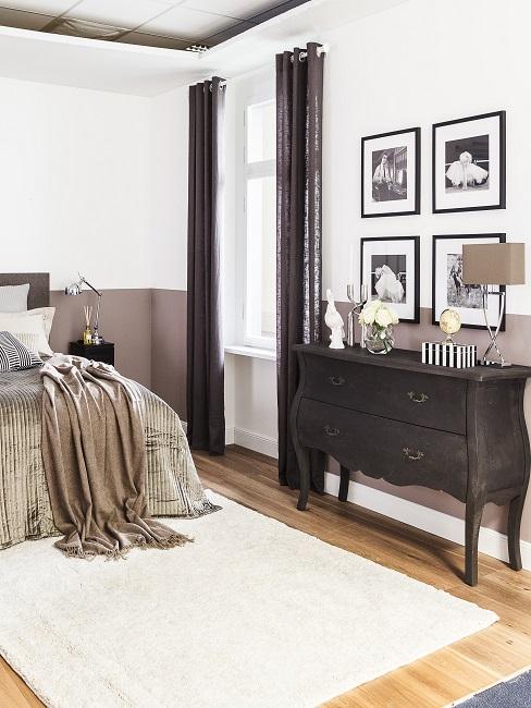 Letto accanto ad una credenza d'epoca, sopra quattro quadri come galleria murale, parete in grigio-bianco