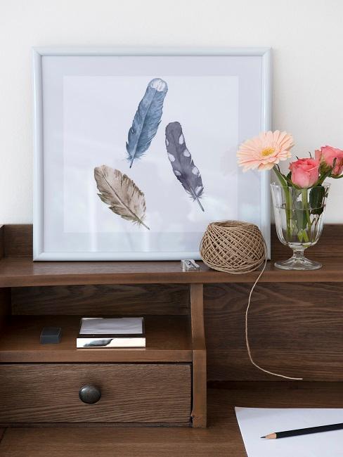 Meuble en bois vernis Bureau en bois foncé avec une impression encadrée de plumes, à côté d'un vase de fleurs