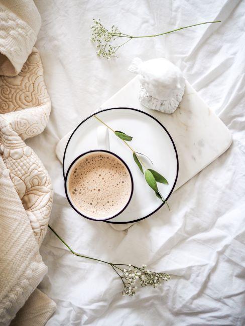 Tendances Pinterest Une tase de café au lait posée sur une sous-tasse blanche posée sur un lit drapé des draps blancs